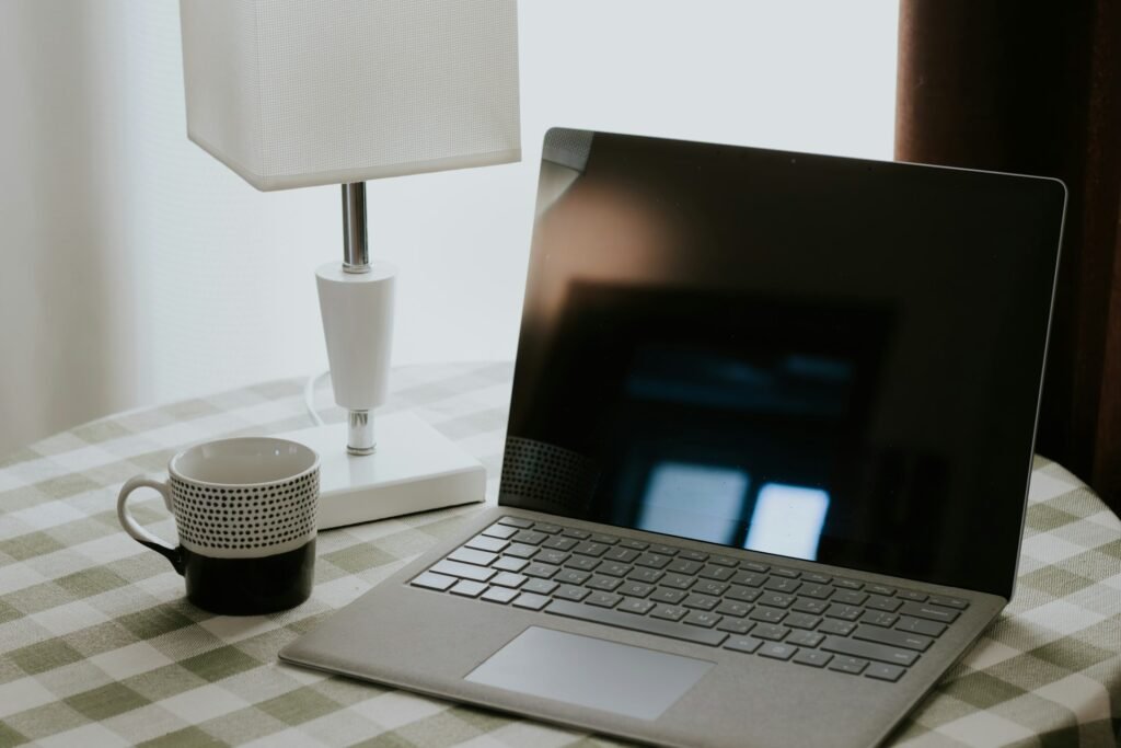 A single laptop, lamp and coffee cup on a simple checked tablecloth