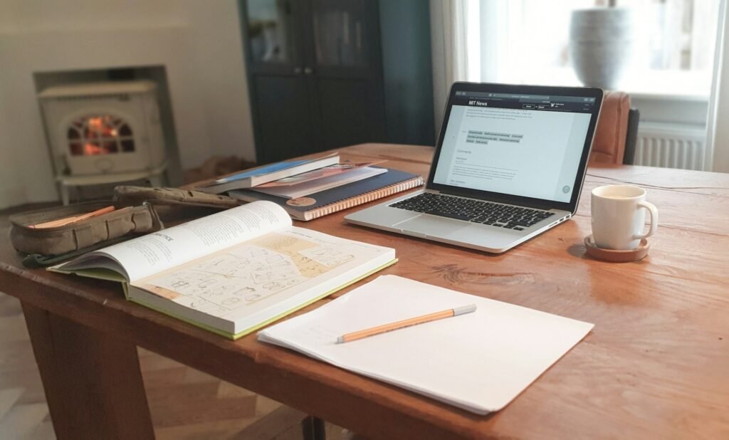 The Money Toolkit for People Who Work From Anywhere (2026 Guide) Laptop, open notebook and coffee mug on a wooden table in a cozy home office