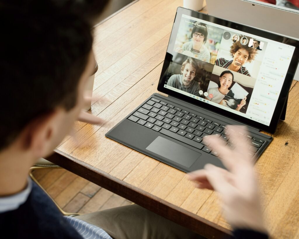 Person on a video call with colleagues on a laptop at a wooden table